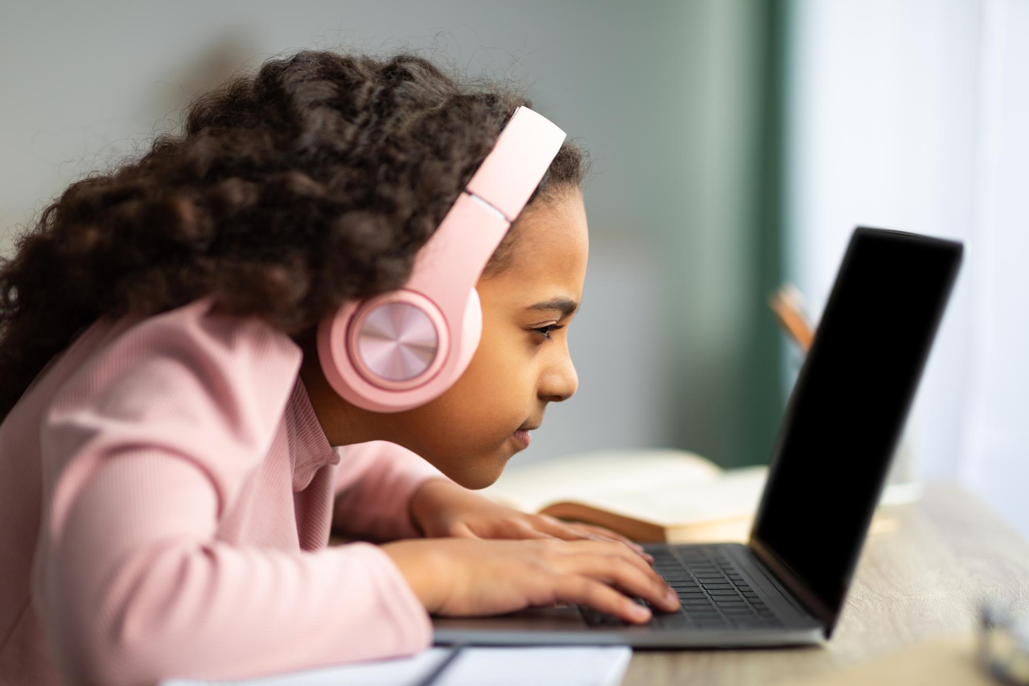 Young girl looking closely at her laptop with headphones on. 